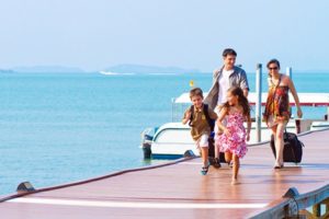 Family with suitcases walking down a pier away from a boat.