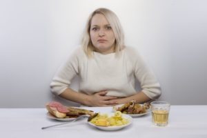 Woman who has an upset stomach from overeating and surrounded by food.