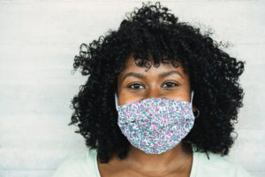 Happy black girl smiling under protective face mask - Young millennial person during coronavirus lifestyle - Health care and happiness concept - Focus on face